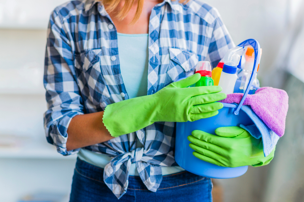 Commercial cleaner wearing green gloves and holding bucket of spray bottles