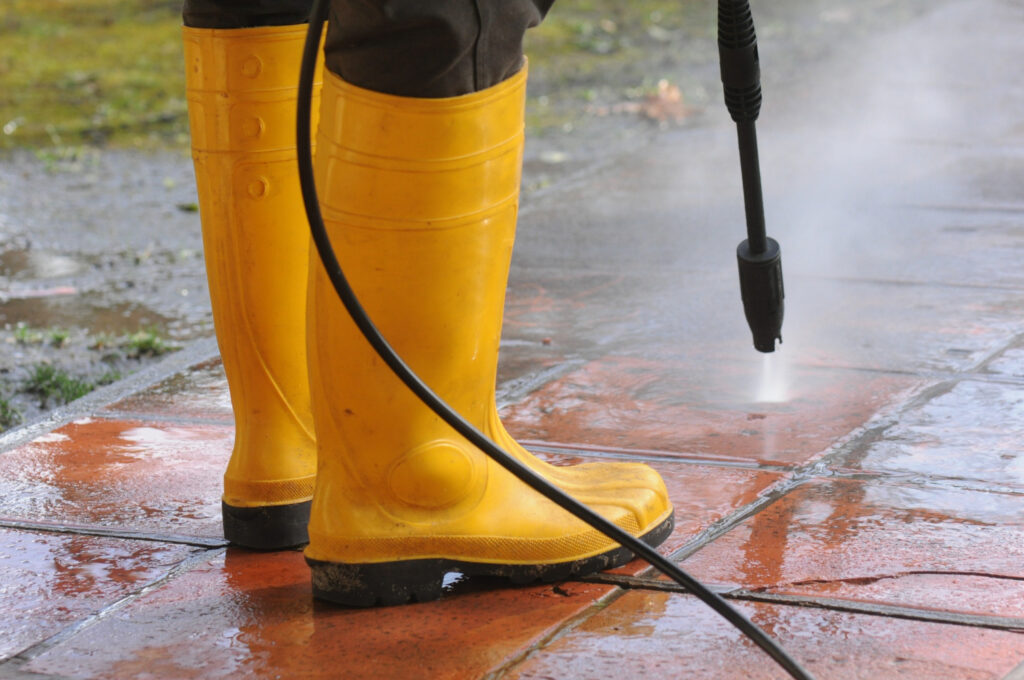 Person in yellow boots power washing a walk